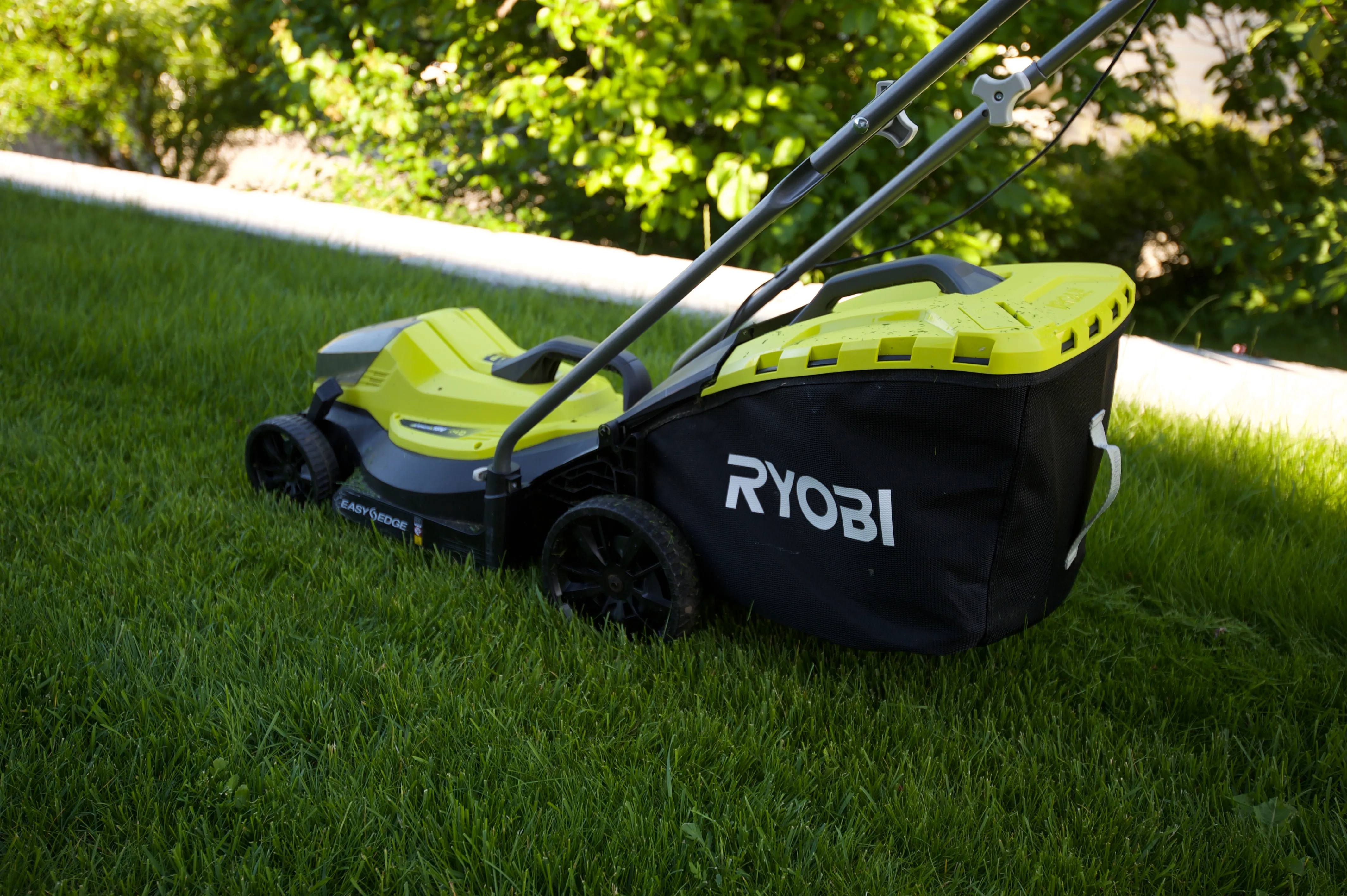 Gressklipper med oppsamler som står i kanten av en nyklipt plen